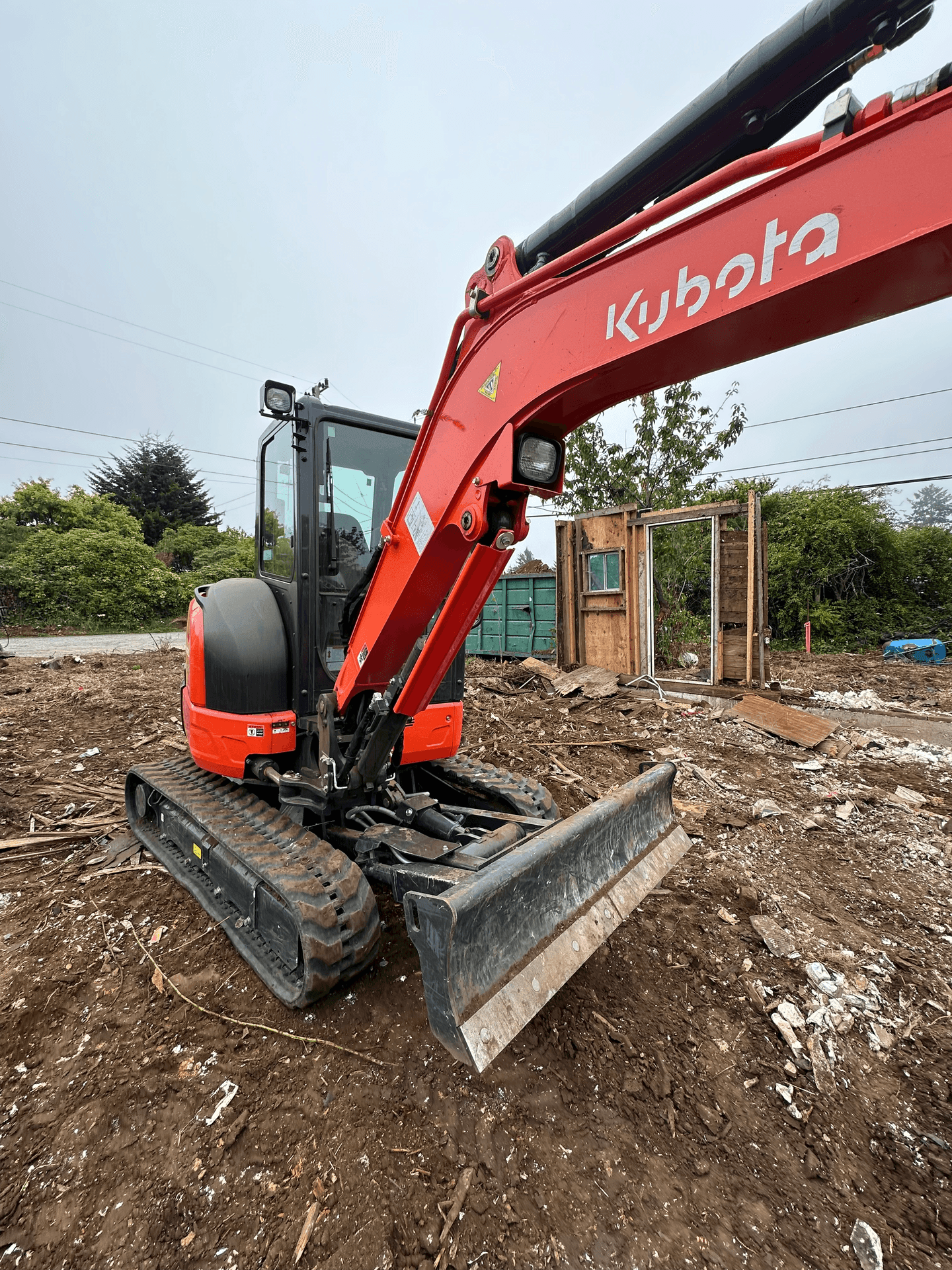 Red excavator on a construction site with muddy ground and debris.